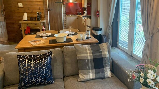 Un ambiente accogliente con un tavolo da pranzo in legno apparecchiato per due persone, un divano con cuscini decorati e una finestra con tende.
