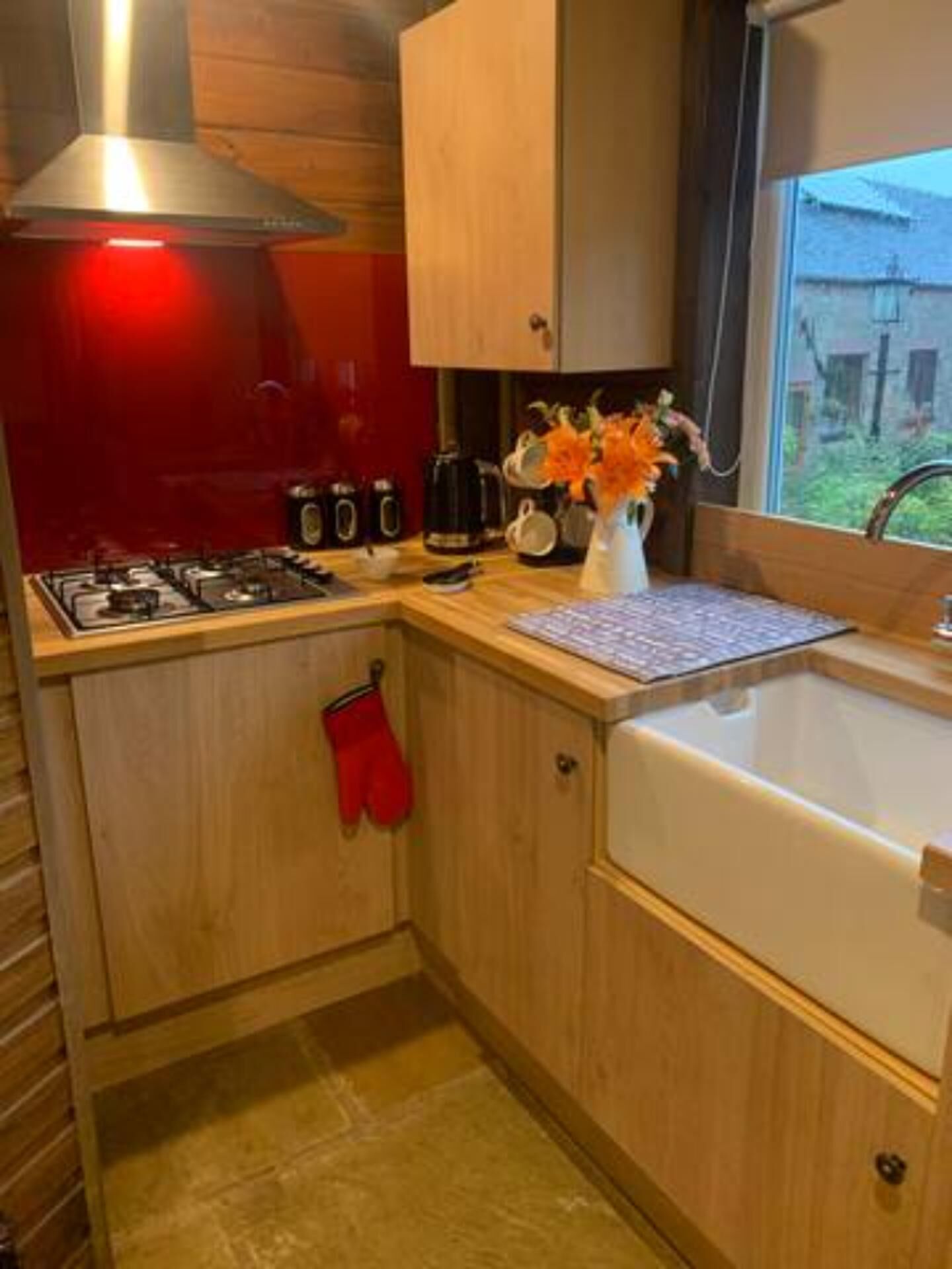 A compact kitchen with wooden cabinets, a gas stove, a coffee maker, and a window with a view of the outside.