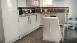 A modern kitchen with white cabinets, a microwave, and a glass dining table. - Charming 1-bed & Balcony Flat in Merthyr Tydfil (Merthyr Tydfil)