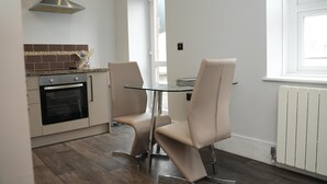 A modern kitchen with a built-in oven, a glass table, and two chairs. - Charming 1-bed & Balcony Flat in Merthyr Tydfil (Merthyr Tydfil)