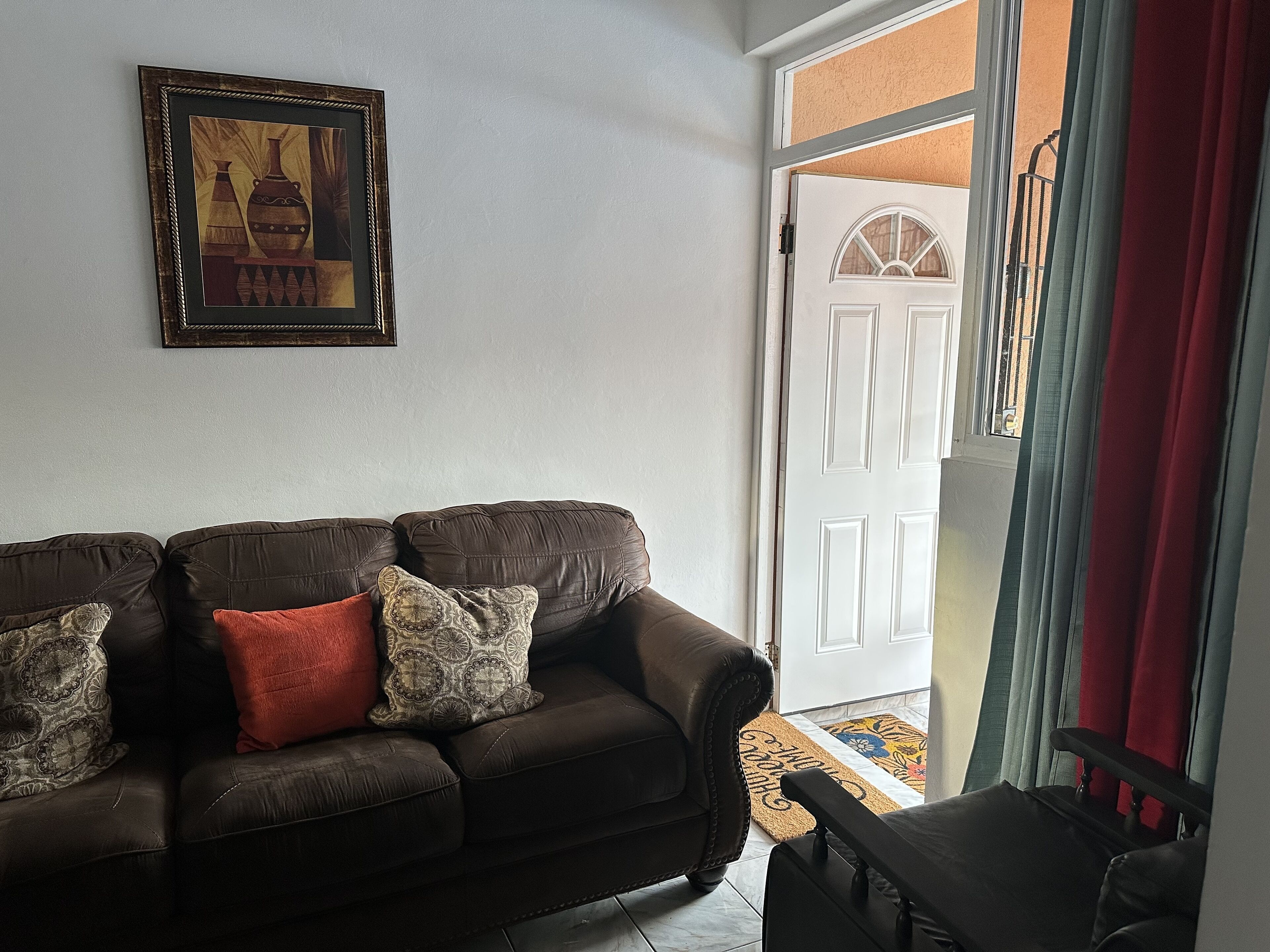 A living room with a dark brown leather sofa, patterned cushions, and a framed artwork on the wall.