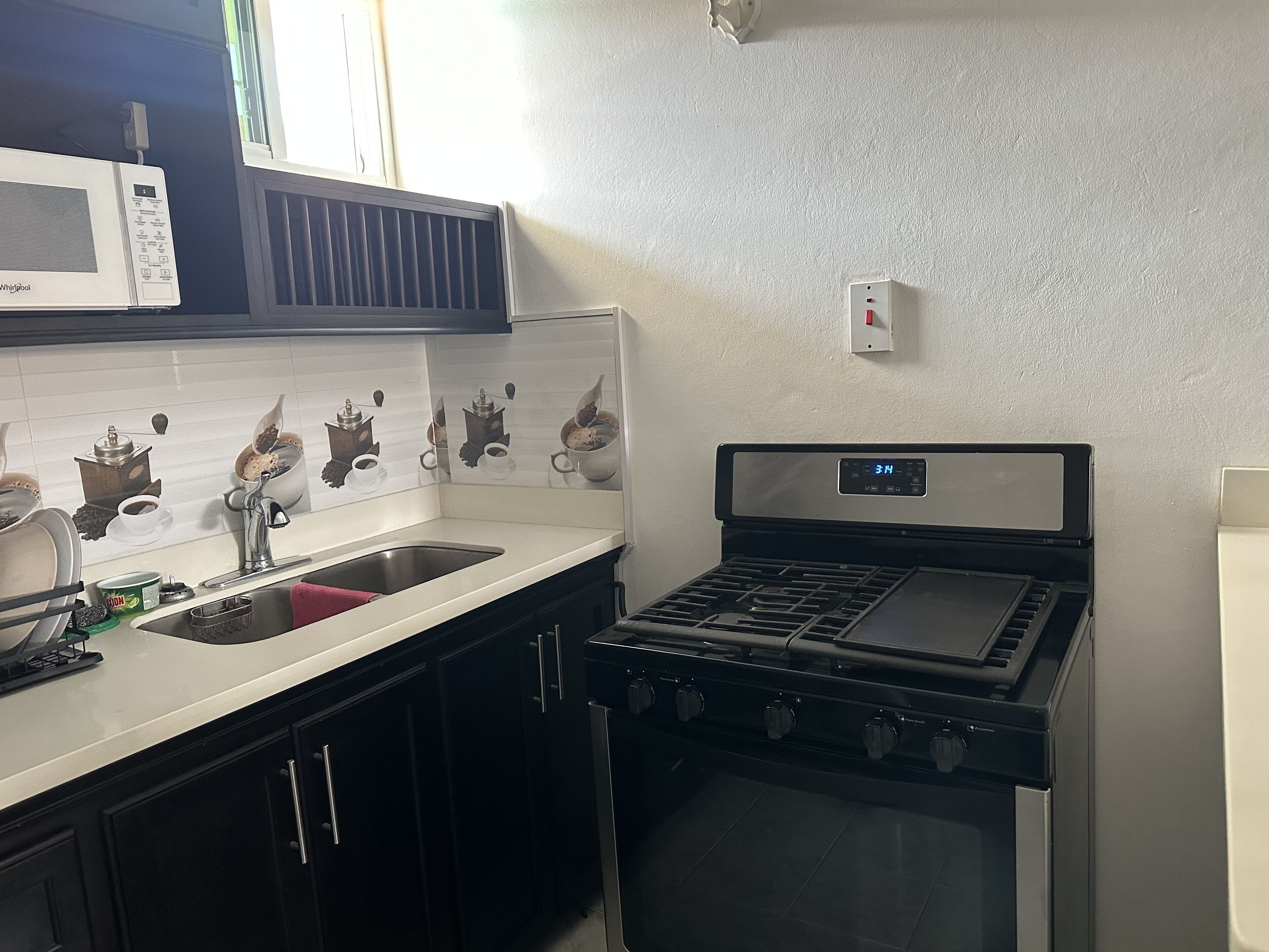 A kitchen with a stove, sink, and microwave. There are cabinets and a window above the sink.