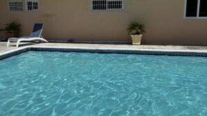 A clear swimming pool with a blue edge, a lounge chair, and potted plants. - Remarkable 1-bed Apartment in Montego Bay (Montego Bay)