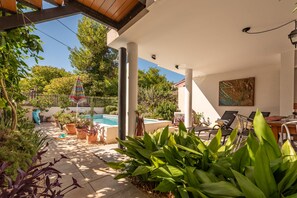 Espaço ao ar livre coberto com piscina, plantas em vasos e área de estar com mesa e cadeiras.