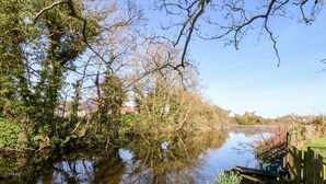 Un río tranquilo con reflejos de árboles y una cerca de madera a la derecha.