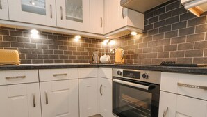 Una cocina moderna con armarios blancos, salpicadero de baldosas negras y horno empotrado.