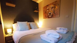 Une chambre d’hôtel avec un grand lit, deux tables de chevet, un tableau représentant un lion et une lampe.