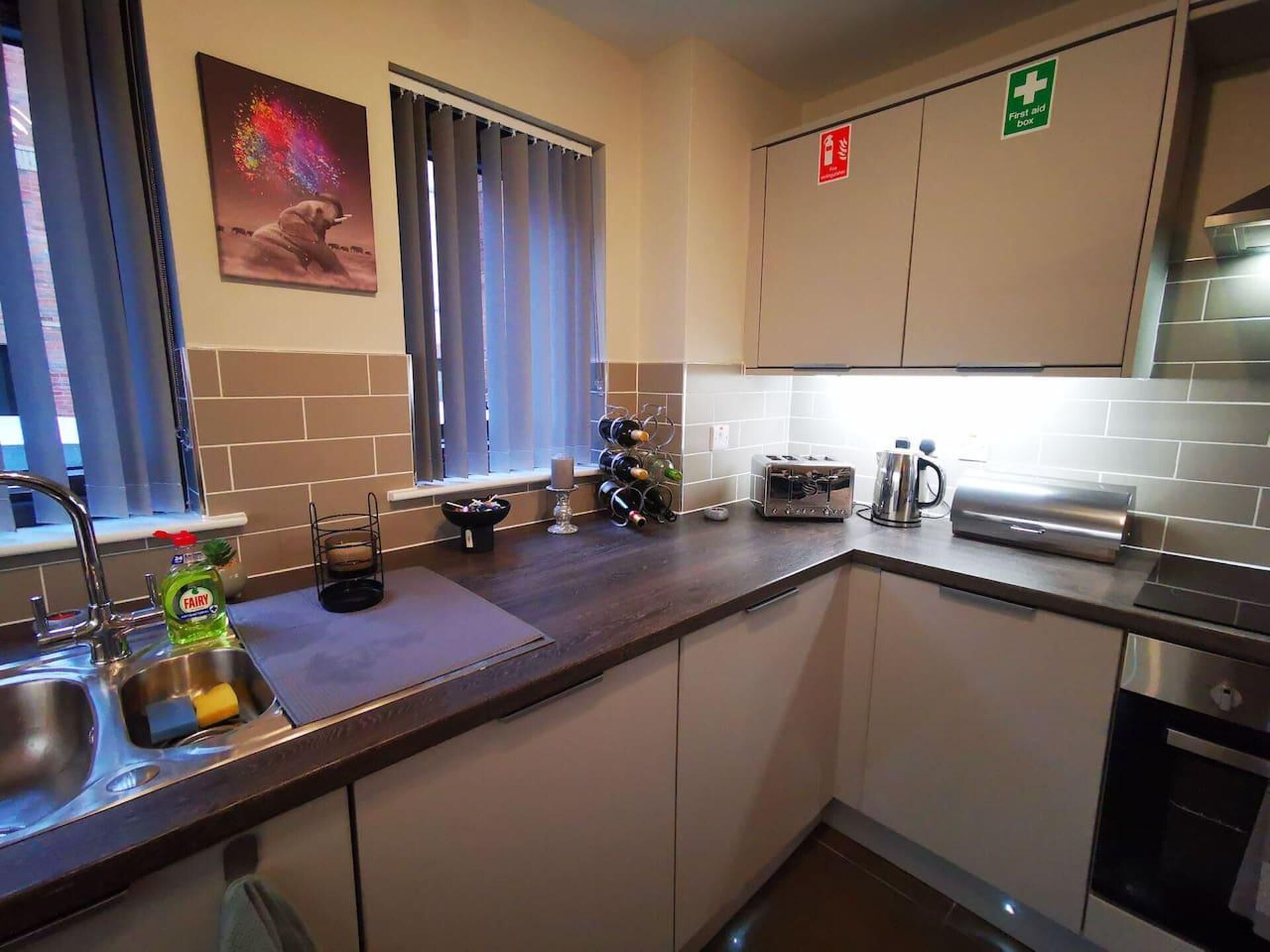 A compact kitchen with a sink, a toaster, a kettle, and a wine rack.