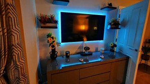 Un salon moderne avec un téléviseur à écran plat fixé au mur, un meuble en bois en dessous et des plantes décoratives disposées sur des étagères murales.