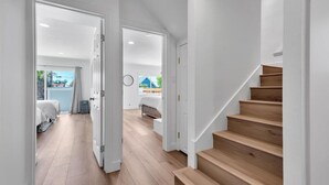 Un interior modern amb una escala de fusta, un passadís que condueix a un dormitori i vista exterior.