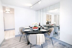 Un comedor moderno con una mesa redonda dispuesta para cuatro personas, un frutero, copas de vino y una botella de vino.