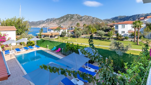 A pool area with lounge chairs and umbrellas, surrounded by greenery and a view of mountains. - Lavinya Selimiye Buotique Hotel (Marmaris)