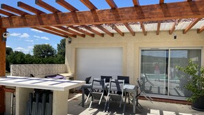 An outdoor patio with a pergola, a table and chairs, a sliding glass door, and a potted plant.