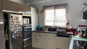 A modern kitchen with stainless steel appliances, a window with blinds, and a tiled floor.
