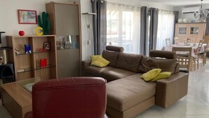 A living room with a brown sofa, red armchair, and a glass coffee table. There is a wooden bookshelf with alphabet letters and a cactus.