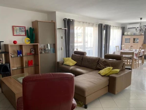 A living room with a brown sofa, red armchair, and a glass coffee table. There is a wooden bookshelf with alphabet letters and a cactus.