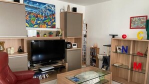 A living room with a flat-screen TV, a red leather chair, a glass coffee table, and a bookshelf with alphabet decorations.