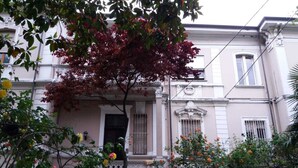 Un immeuble à la façade de style traditionnel, doté d’un balcon avec une balustrade et d’un petit jardin agrémenté de fleurs.