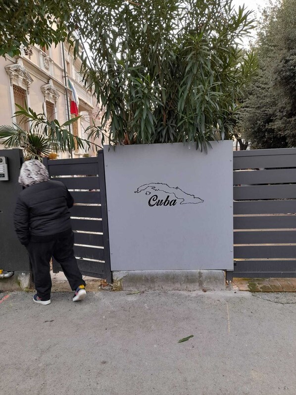 Une personne qui passe devant une grille sur laquelle est affiché un panneau indiquant « Cuba » et sur laquelle on peut voir le contour d’une carte.