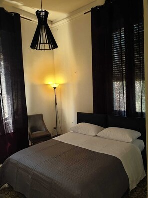 Une chambre à coucher avec un lit, une chaise, une lampe sur pied et une fenêtre avec des stores.