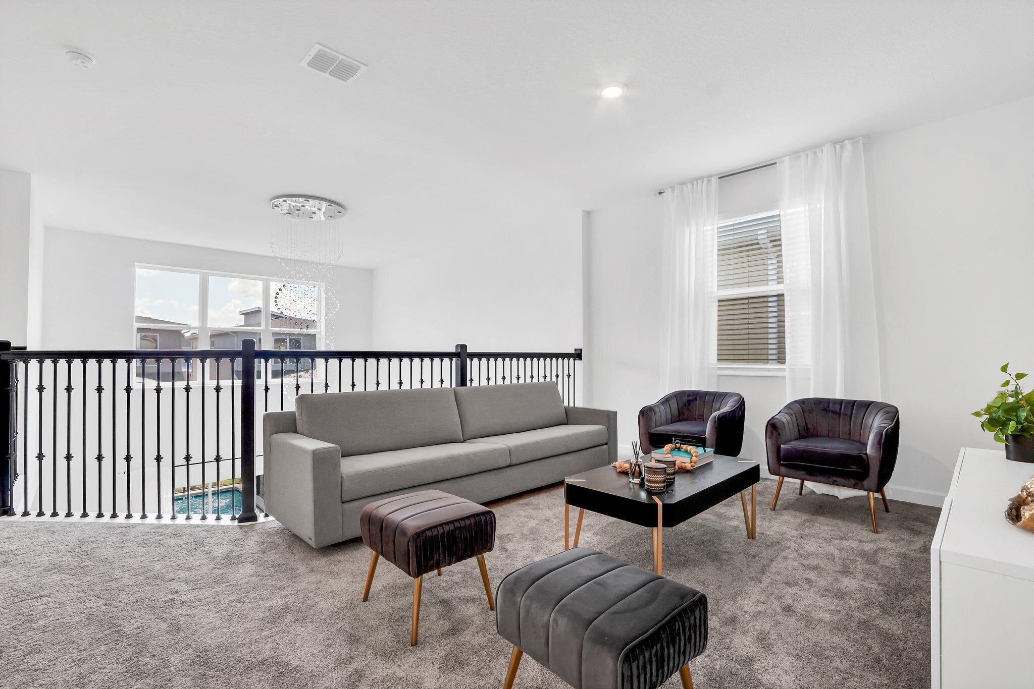 A modern living room with a grey sofa, two armchairs, a coffee table, and a small ottoman. A balcony with a railing is visible in the background.