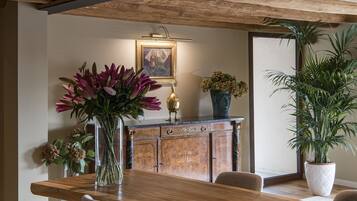 Un comedor con mesa de madera, sillas, un jarrón de flores, un aparador con un cuadro y una planta en maceta.