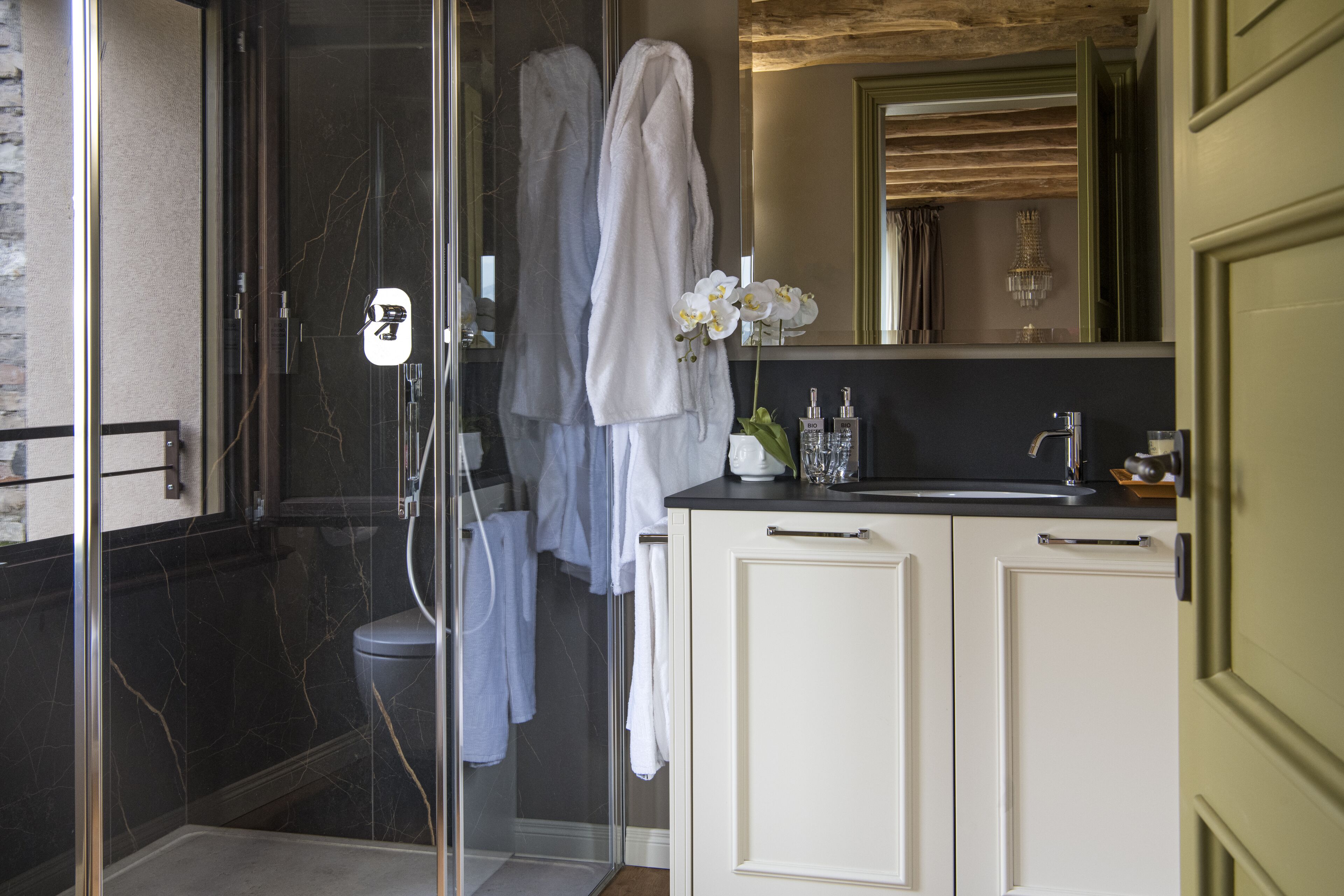 A bathroom with a glass shower enclosure, a white bathtub, a vanity with a mirror, and a vase with flowers.