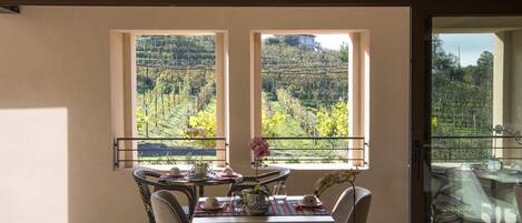 Un comedor con una mesa dispuesta para cuatro, dos ventanas grandes que dan a un viñedo y un balcón con barandilla de vidrio.
