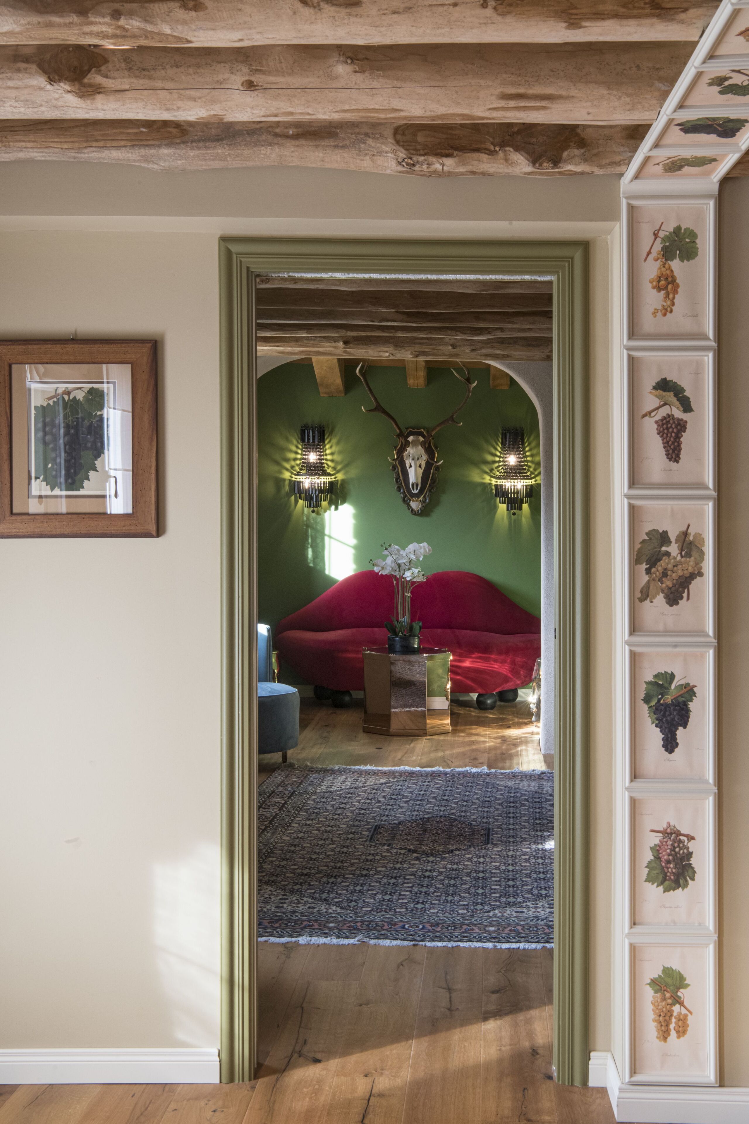 Um quarto com sofá vermelho, teto de madeira e parede verde com gravuras botânicas emolduradas.