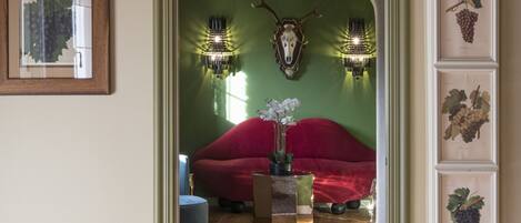 Um quarto com sofá vermelho, teto de madeira e parede verde com gravuras botânicas emolduradas.