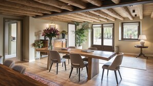 Un vaste espace dédié à la salle à manger, avec une table et des chaises en bois, une plante en pot et une vue sur l’extérieur grâce à de grandes fenêtres.