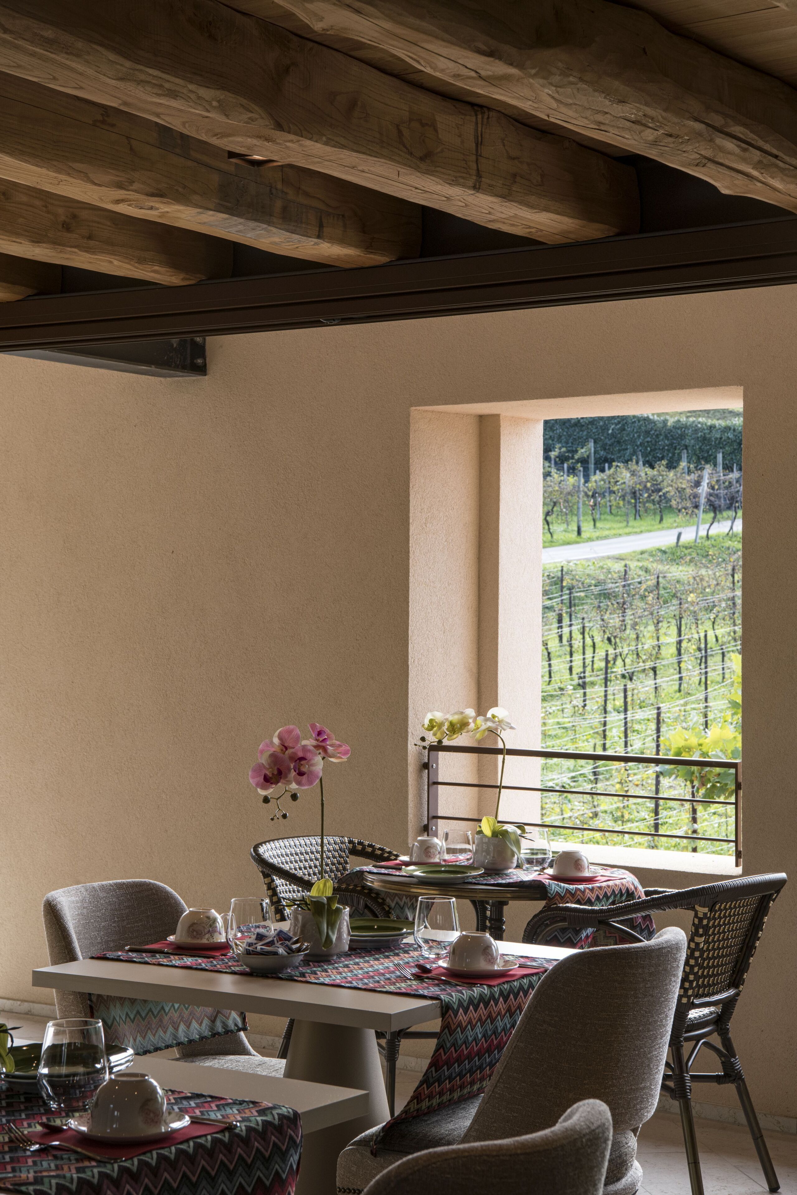 Ein Essbereich mit Tisch für vier Personen, Stühlen und Blick auf einen Weinberg durch ein Fenster.