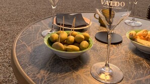 Une table avec deux verres à vin, un saladier de fruits et une lampe, sur une terrasse offrant une vue sur les montagnes.