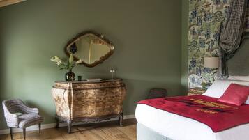 A bedroom with a wooden dresser, a mirror, a bed with a red blanket, and a chair.