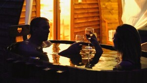 Una pareja sentada a una mesa con una copa de vino, en una habitación con paredes de madera y un ventanal.