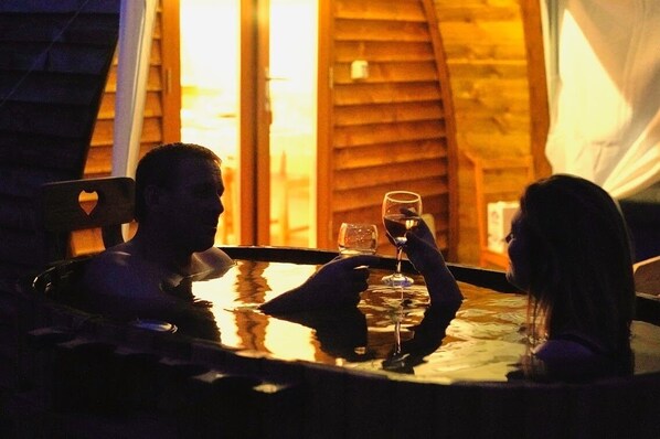 A couple sitting at a table with a glass of wine, in a room with wooden walls and a window.