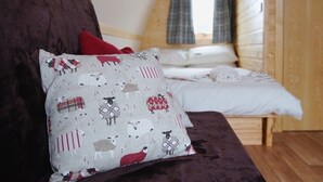 Un dormitorio acogedor con una cama, un almohadón con estampado de ovejas y una ventana con cortinas.