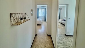 A hallway leading to a bedroom with a bed, a small table, and a wall-mounted shelf with plants. - Bright apartment for a pleasant stay in Hyères (Hyères)