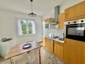 Eine Küche mit Holzschränken, einer Mikrowelle, einem Backofen, einem Spülbecken und einem Esstisch mit Stühlen.