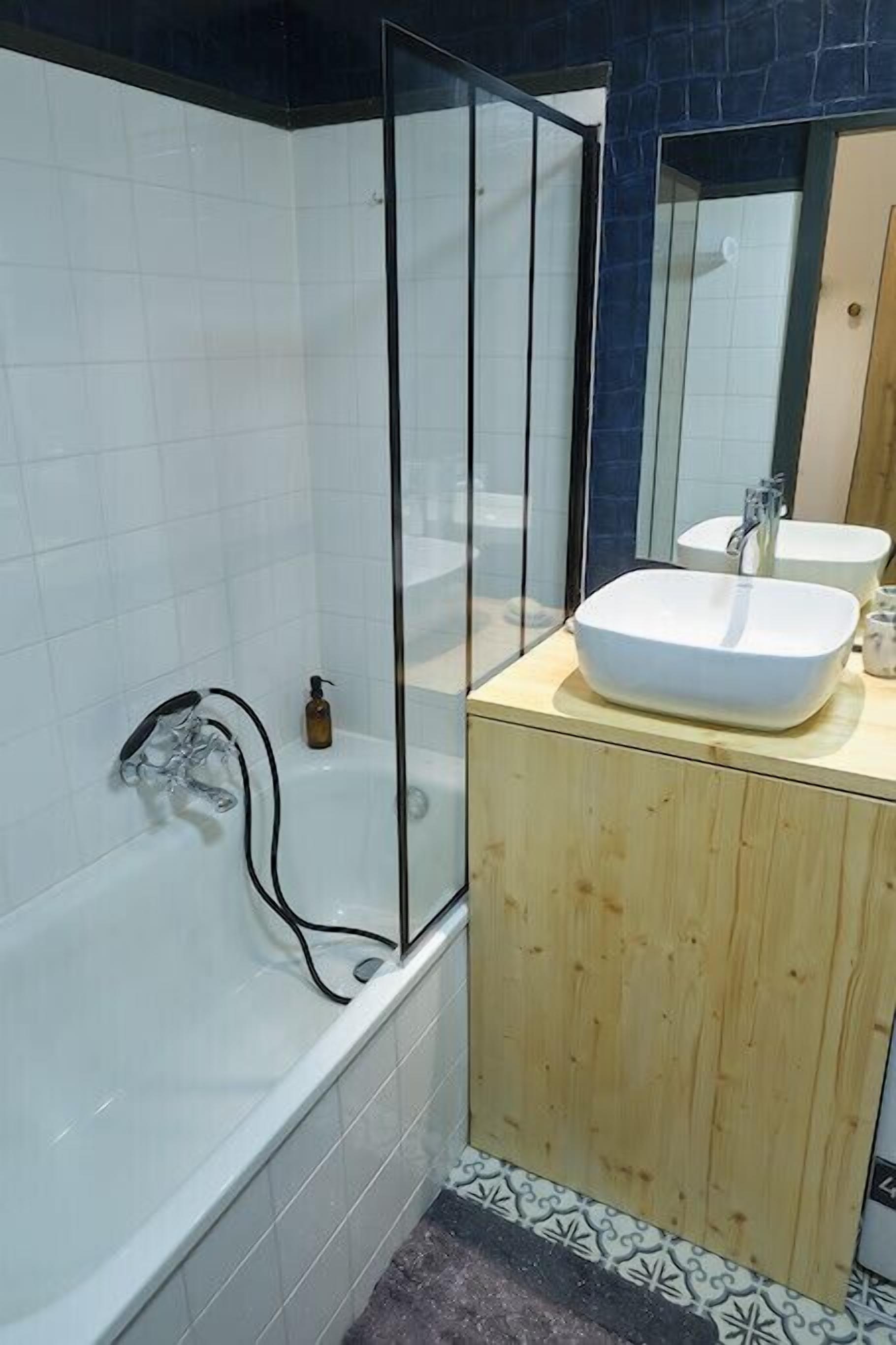 Een moderne badkamer met een douchecabine van glas, een witte badkuip en een houten wastafelmeubel met twee wastafels.