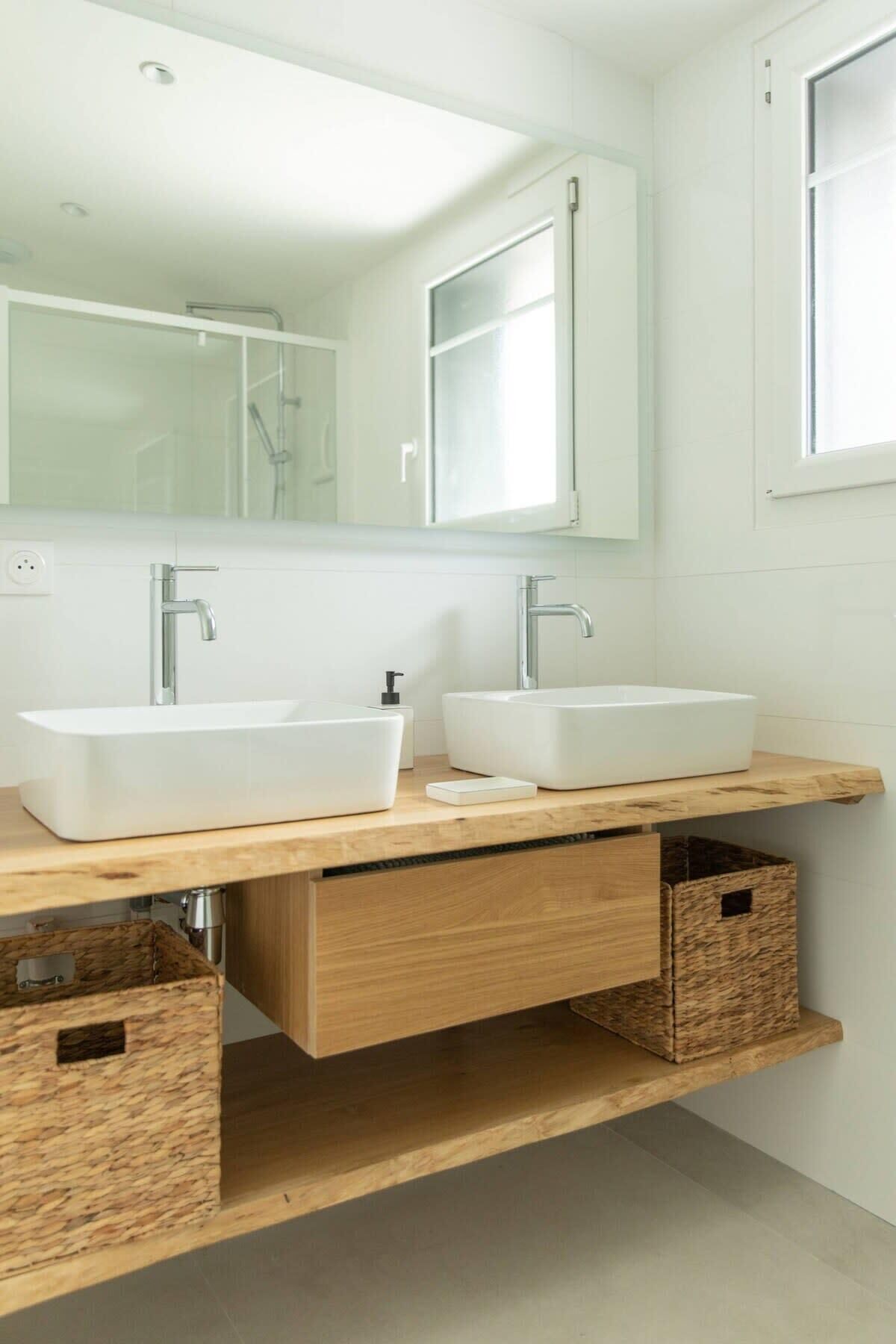 Un baño moderno con dos lavamanos blancos tipo pedestal, un espejo grande y cajones de almacenamiento de madera.