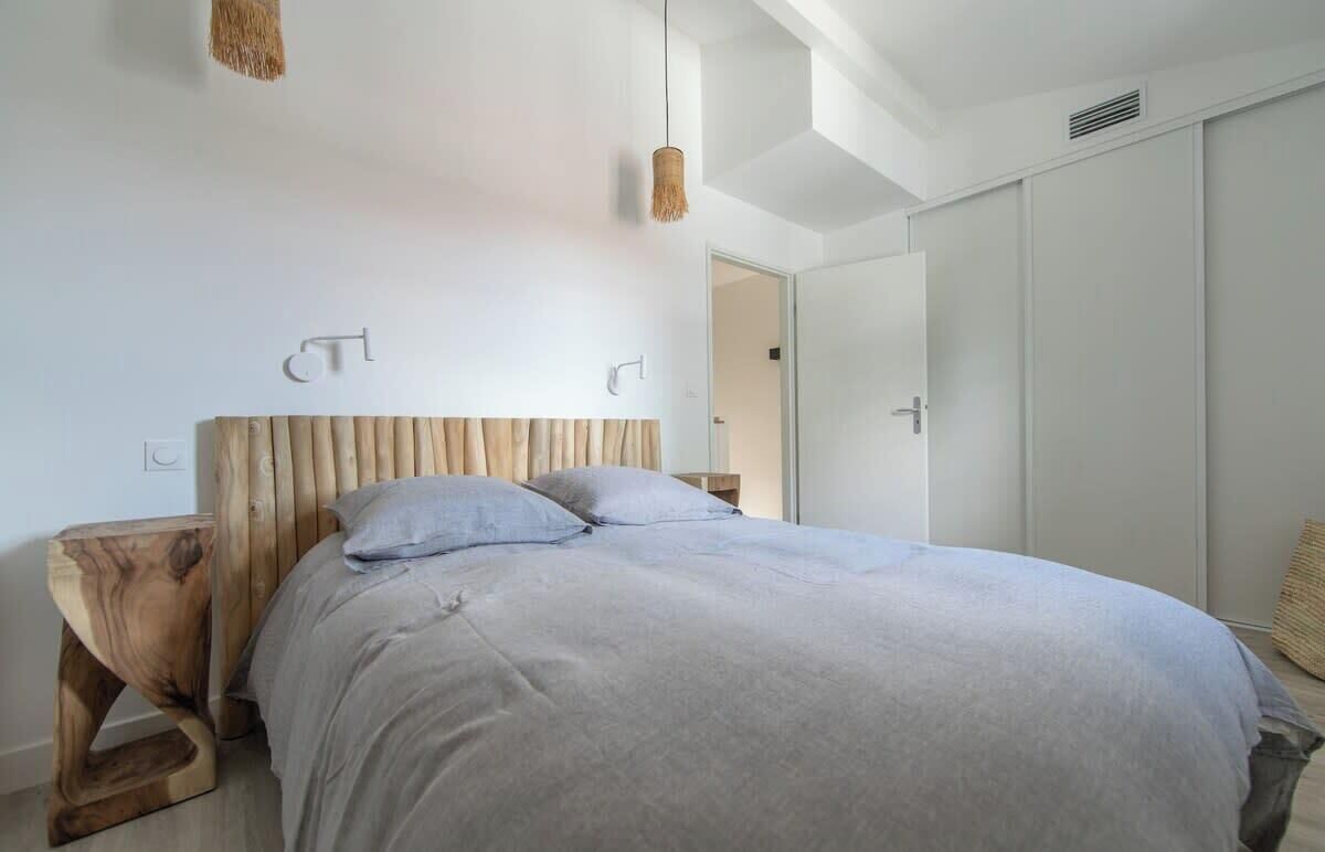 A bedroom with a wooden headboard, a bed with grey bedding, a hanging light fixture, and a wardrobe.