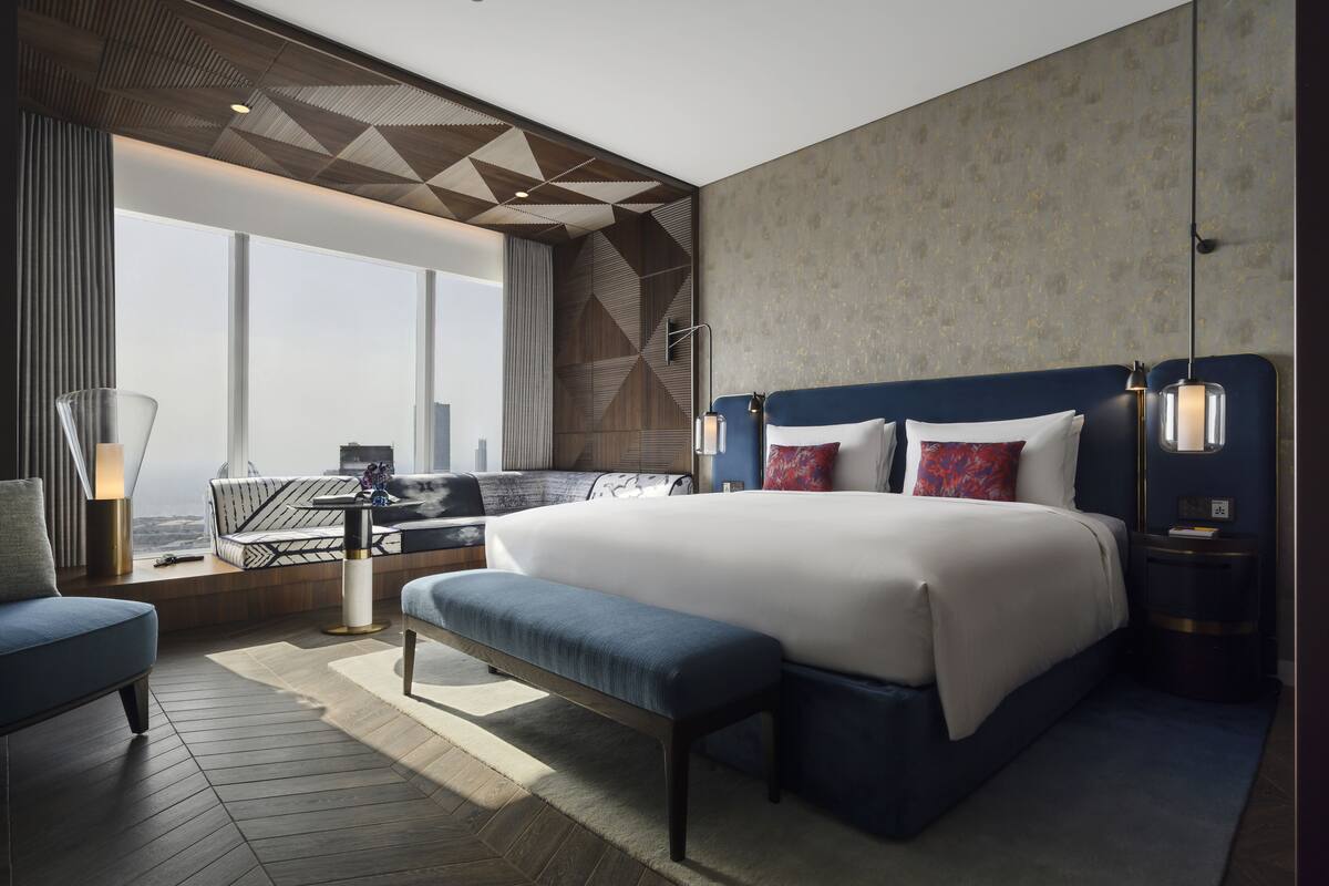 Een moderne hotelkamer met een groot bed, een zithoek met uitzicht en een geometrisch plafondontwerp.