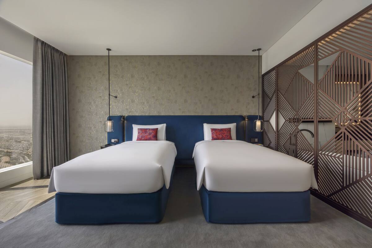 Een hotelkamer met twee bedden, een groot raam en een decoratief wandpaneel.
