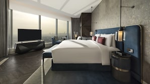 A modern hotel room with a large bed, a flat-screen TV, a side table, and a view of the city.