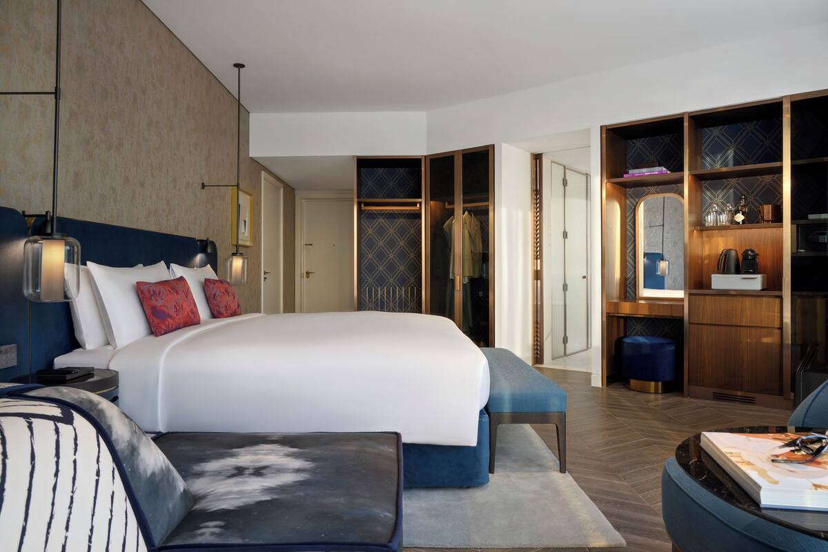 Een moderne hotelkamer met een groot bed, een zithoek met een salontafel, een kledingkast met ingebouwde planken en een spiegel.