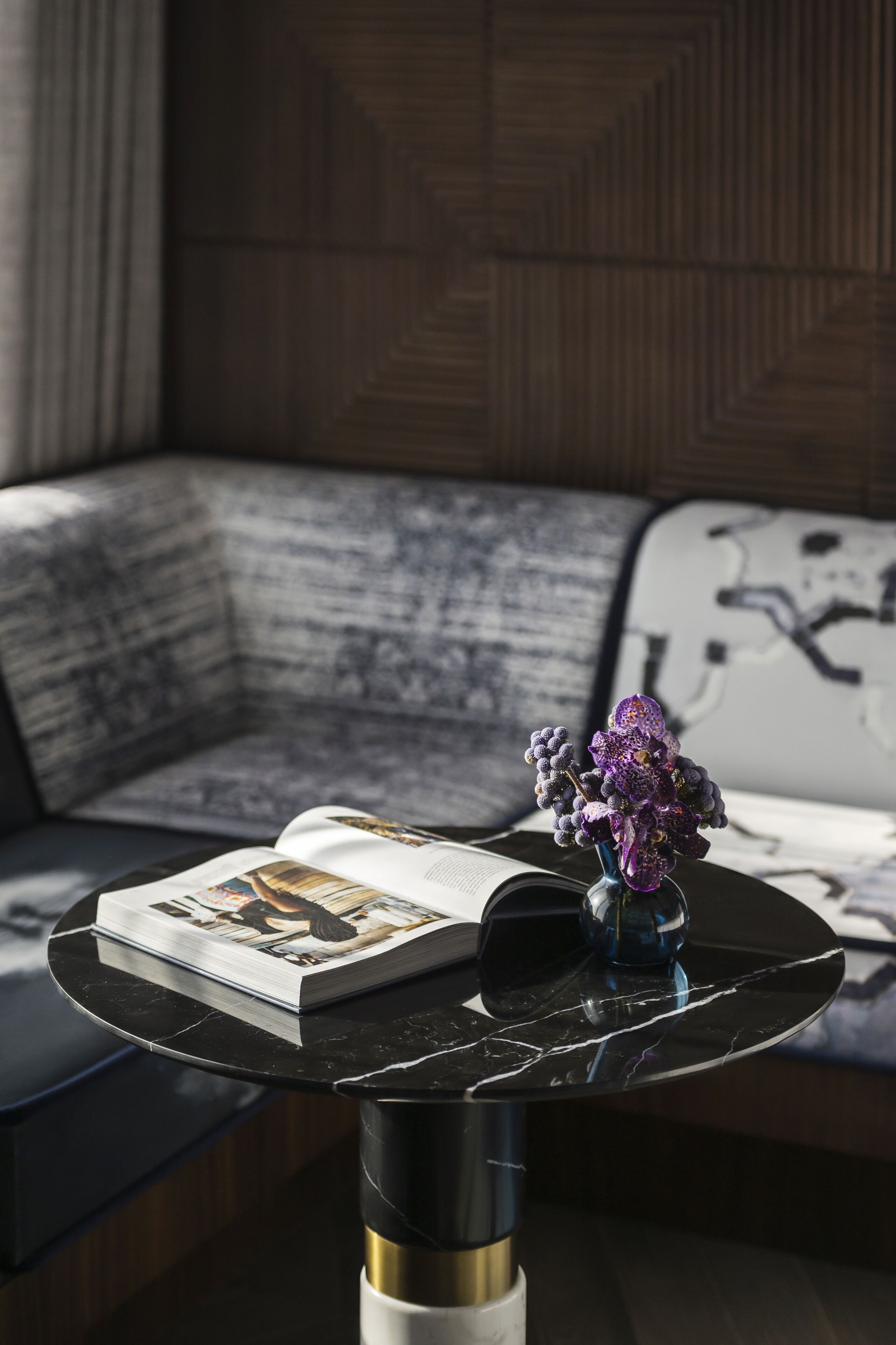 A modern living room with a black marble coffee table, a magazine, and a vase with purple flowers.