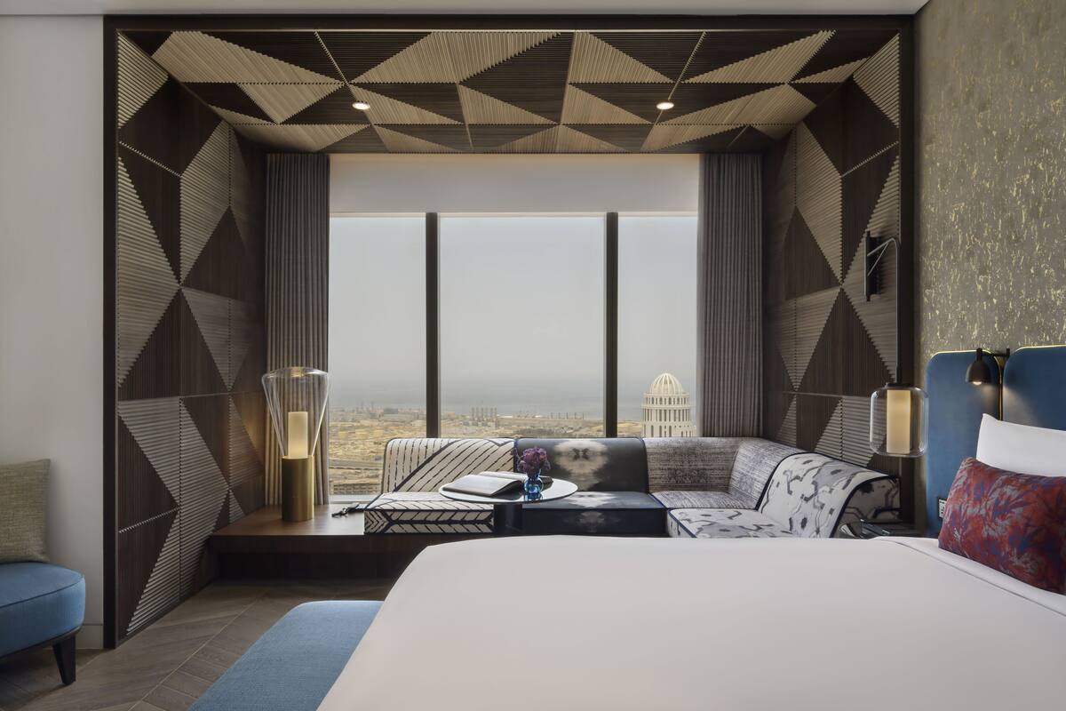 Een moderne hotelkamer met een groot bed, een bank en uitzicht op een stadsbeeld door middel van ramen van de vloer tot aan het plafond.