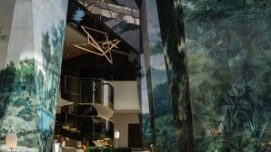 A spacious lobby with a modern design, featuring a large mural of a forest, contemporary seating, and a staircase leading to upper floors.