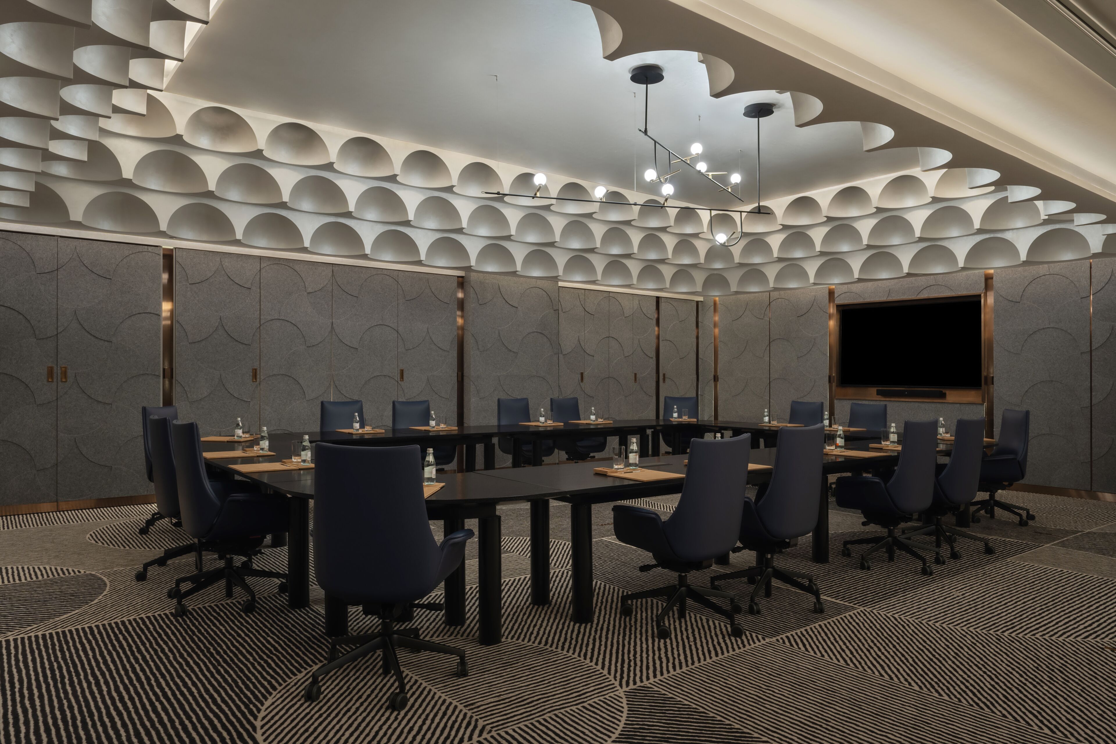 A conference room with a modern ceiling design, a large flat-screen TV, and a long table with chairs.